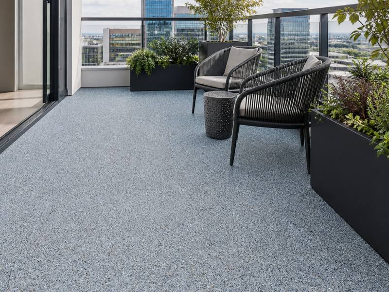 Condo balcony finished in light grey rubber surfacing with two chairs and planters