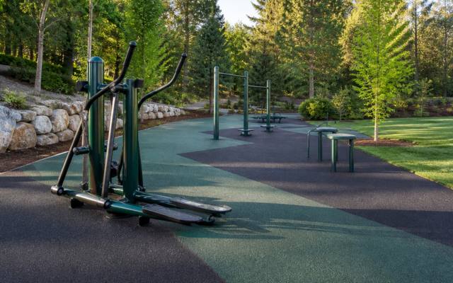 Outdoor fitness machines standing on green and charcoal rubber surfacing in a park